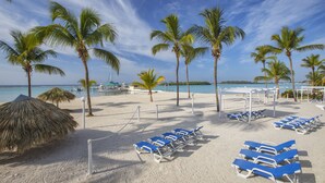 A beach with palm trees, a thatched umbrella, and blue lounge chairs.