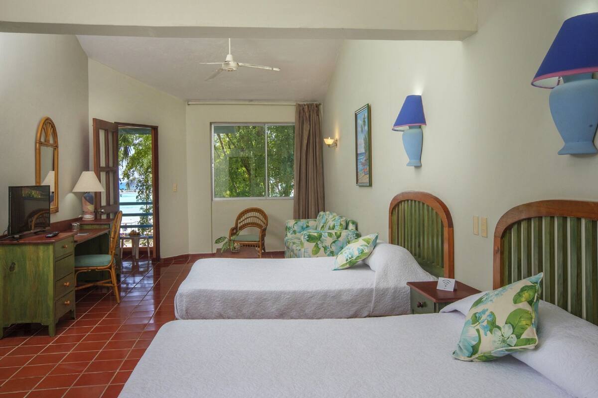 A room with two beds, a desk, a chair, a window with curtains, and a ceiling fan.