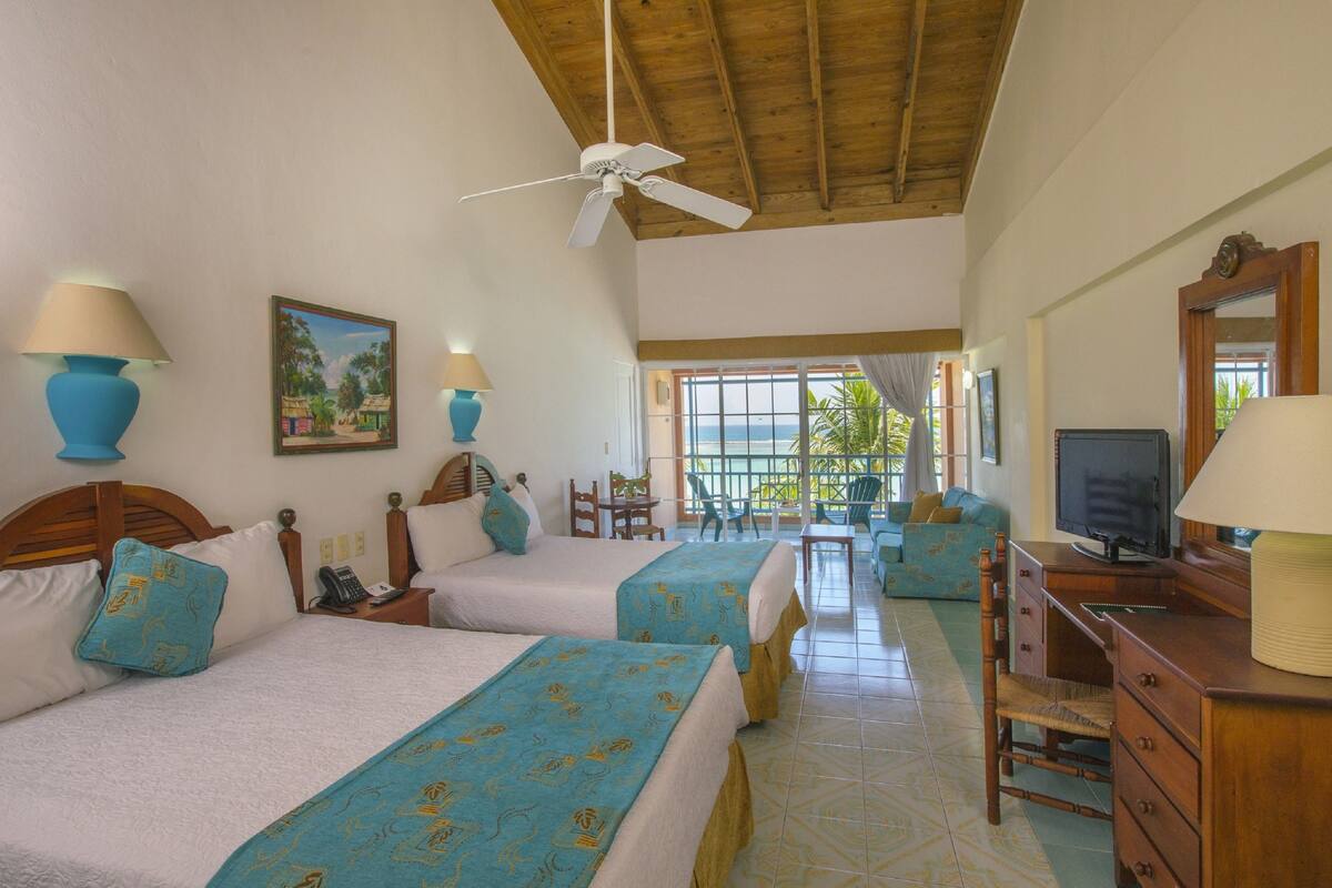 A hotel room with two beds, a TV, a desk, and a balcony with a view.