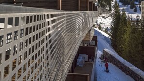 En modern byggnad med en balkong som vetter ut mot ett snöklätt berglandskap.