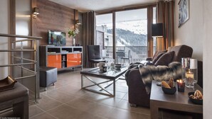 Ett modernt vardagsrum med en soffa, ett soffbord och en tv. En balkong med utsikt över ett snötäckt berg syns genom stora fönster.