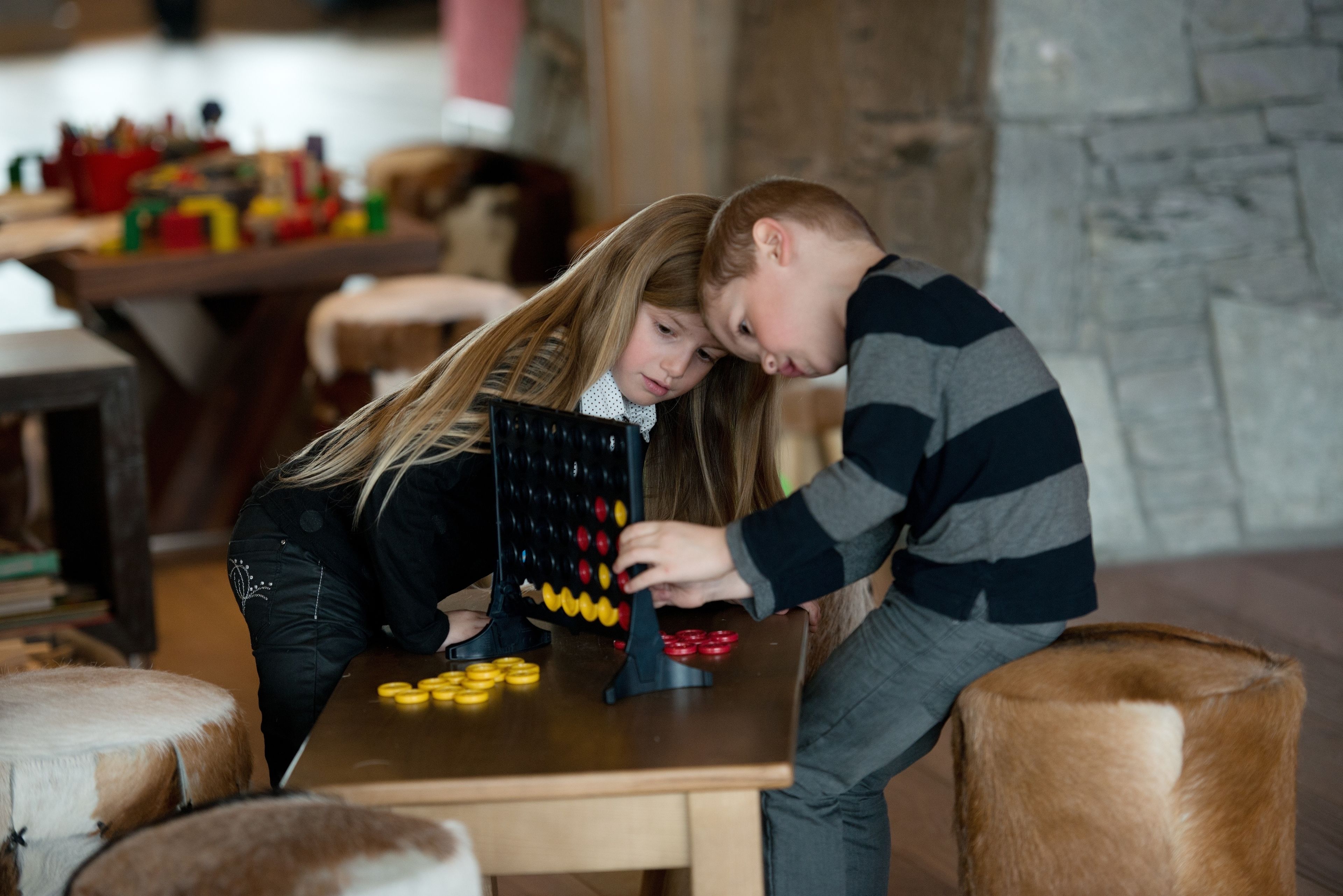 Dos niños jugando con un juego sobre una mesa de madera en una habitación con paredes de piedra y un ambiente rústico.