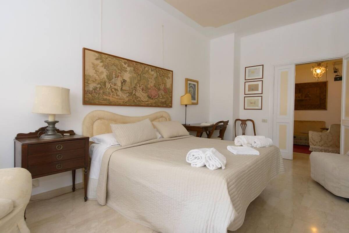 A hotel room with a large bed, a nightstand with a lamp, a chair, and a painting on the wall.
