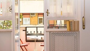 A room with a wooden floor, a bed with a patterned cover, a radiator, and a view of an outdoor seating area with tables and chairs. - Minerva B&B (Rome)