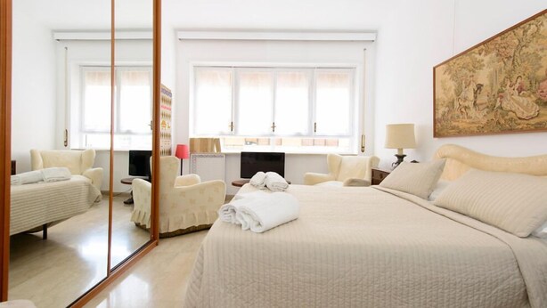 A hotel room with a large bed, a sitting area with a chair and a small table, a television, and a large window with curtains. - Minerva B&B (Rome)
