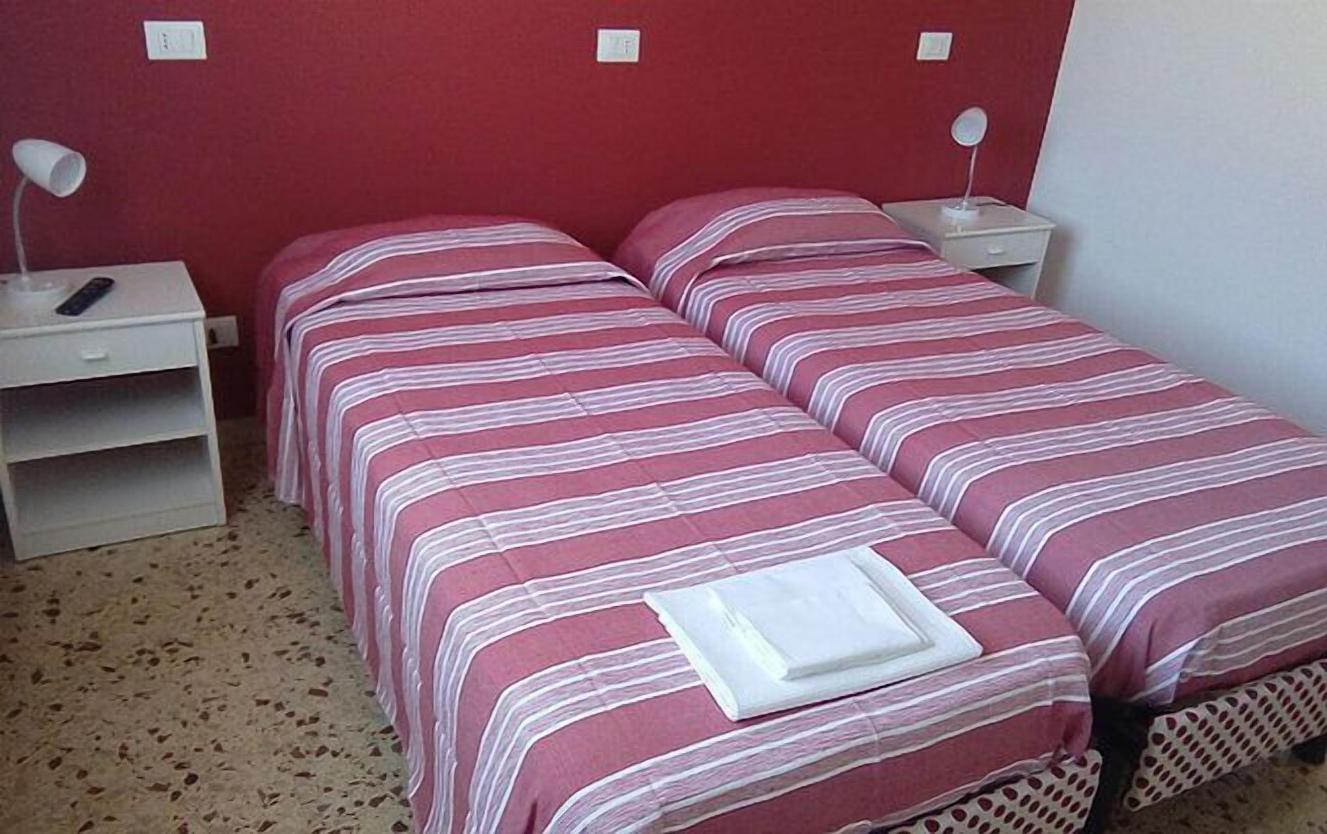 Una cama doble con ropa de cama a rayas en una habitación con pared roja y mesitas de noche blancas.