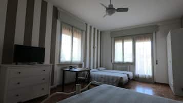 Une chambre d’hôtel comprenant un lit, un bureau, une chaise, une télévision et deux fenêtres avec des rideaux.