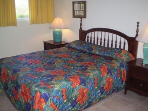 A bedroom with a floral bedspread, two bedside lamps, a wooden headboard, and a framed picture on the wall. - Miramar Villa (Ocho Rios)