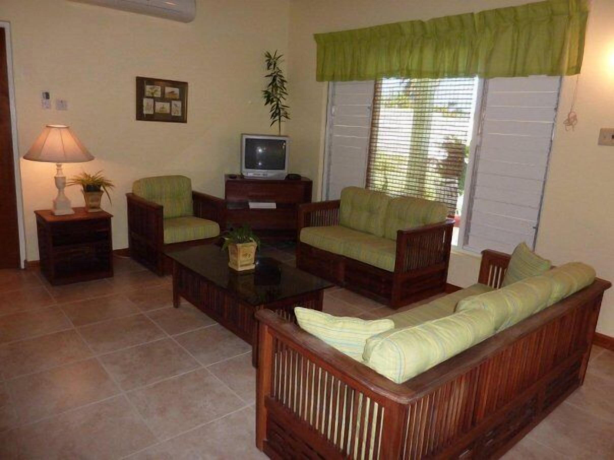 A living room with a sofa set, a coffee table, a television on a stand, a lamp, and a window with blinds.