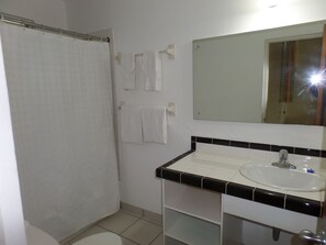 A bathroom with a shower curtain, a sink, a mirror, and two towels hanging on the wall. - Miramar Villa (Ocho Rios)