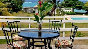A round table with chairs and a vase of flowers on a patio overlooking a pool and ocean view. - Miramar Villa (Ocho Rios)