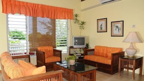 A living room with two orange sofas, a wooden coffee table, and a television on a stand. - Miramar Villa (Ocho Rios)
