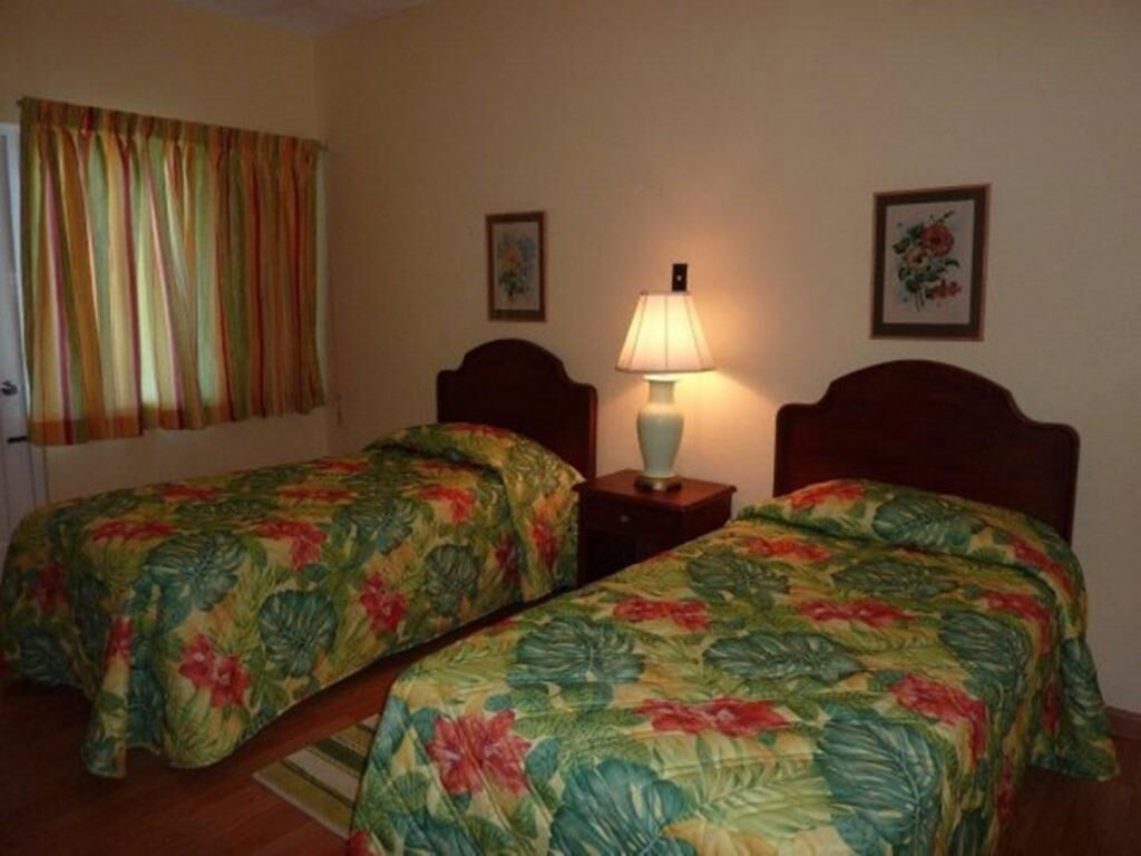 A room with two single beds, a nightstand with a lamp, and a window with curtains.