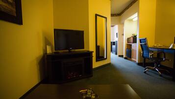 A hotel room with a television, a mirror, a desk with a chair, and a fireplace.