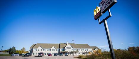 A Chisholm Inn & Suites with a McDonald's sign, multiple cars parked in front, and a clear blue sky.