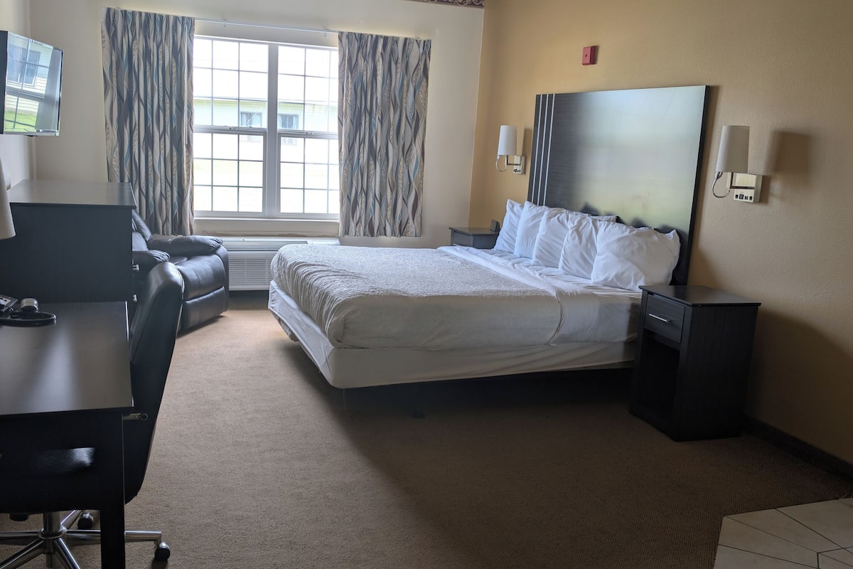 A hotel room with a bed, desk, chair, and a window with curtains.