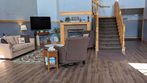 Ein geräumiges Wohnzimmer mit Kamin, großer Uhr, Treppe und Flachbildfernseher.