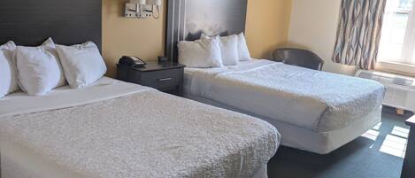 A hotel room with two beds, a desk, a chair, and a window with curtains.