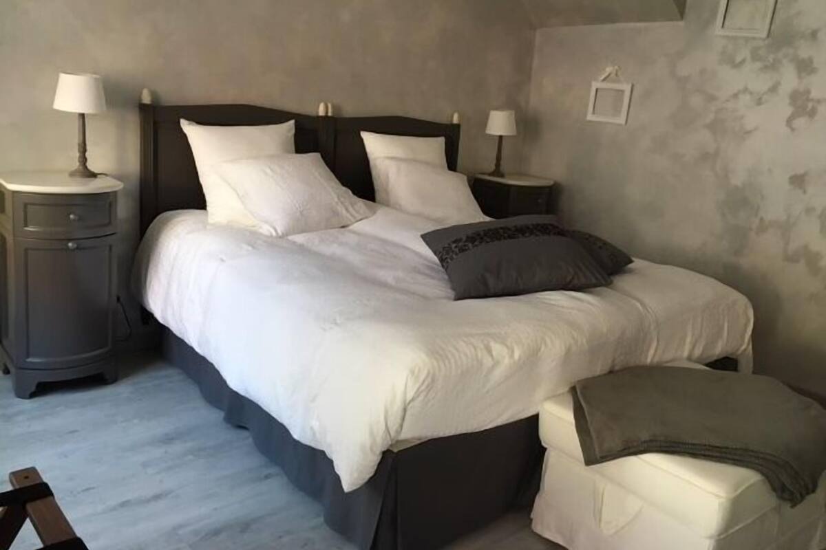 A bedroom with a bed, two bedside tables, a nightstand, and a small bench.