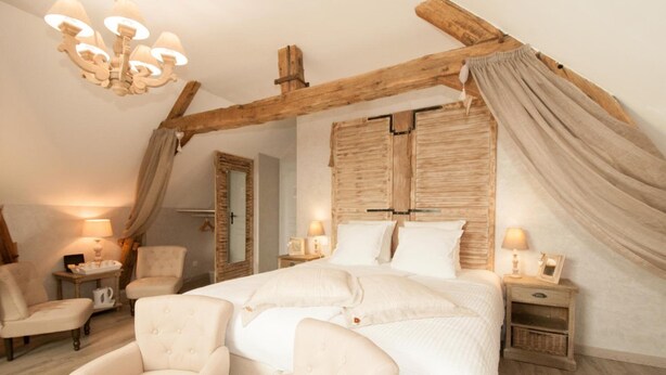 A bedroom with a large bed, wooden beams, a chandelier, and two bedside tables with lamps. - Le Logis Aux Bulles (Verzy)