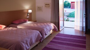 A hotel room with two beds, a wooden headboard, a nightstand with a lamp, and a view of the outside through a glass door. - Casa D'Edite (Chamusca)