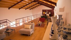 A spacious loft with a high ceiling, a staircase, a seating area with a sofa and armchairs, and a dining area with a table and chairs. - Casa D'Edite (Chamusca)