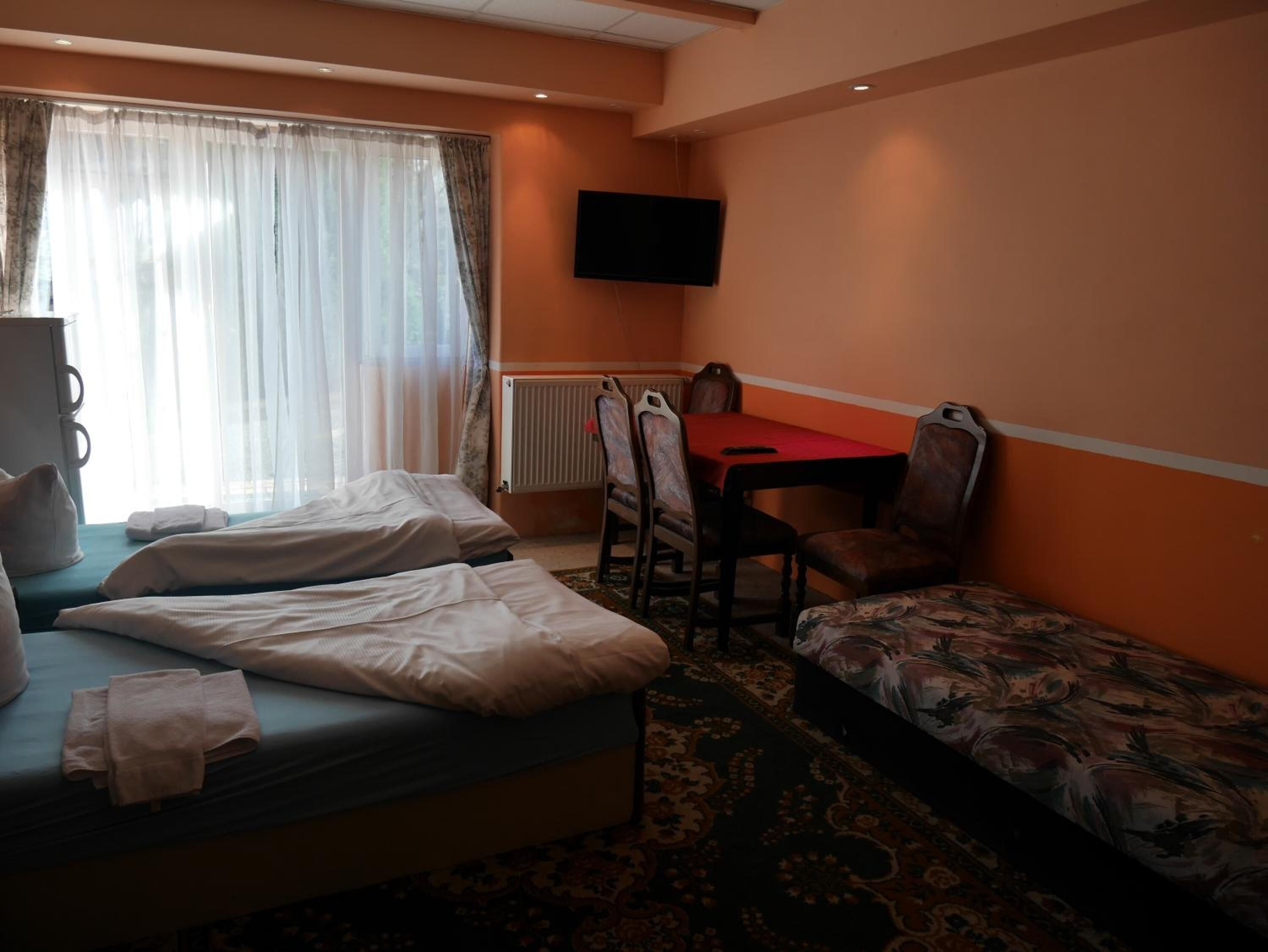 A hotel room with a bed, a small table with chairs, a television, and a window with curtains.
