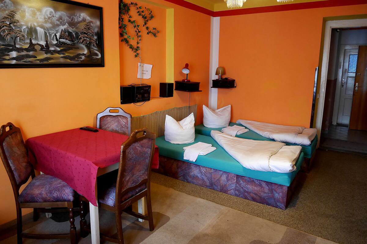 A hotel room with a bed, a desk with a chair, a painting on the wall, and a chandelier.