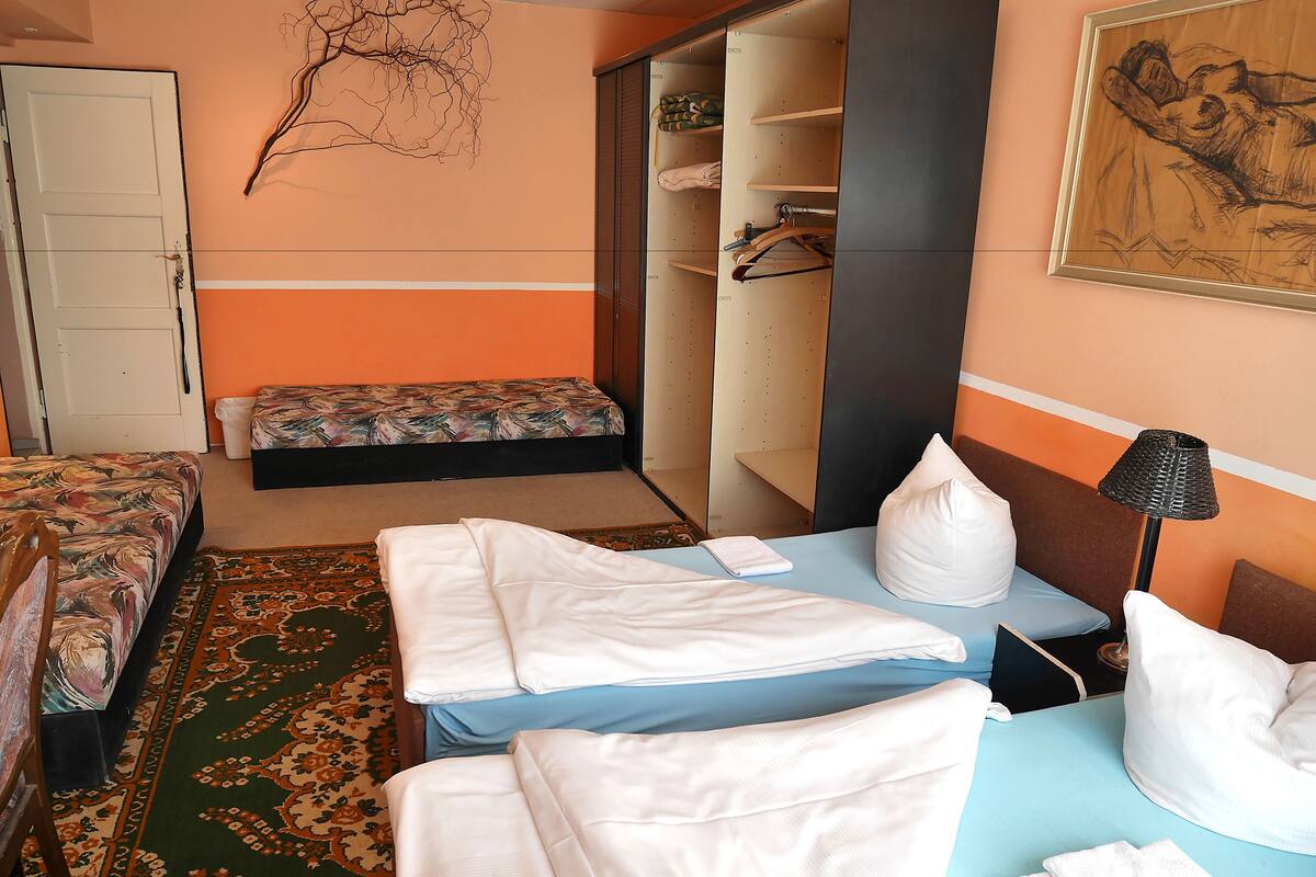 A hotel room with two beds, a bench, a wardrobe, and a painting on the wall.