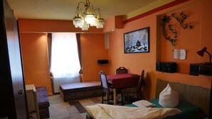 A compact hotel room with two beds, a small table, a bench, and a desk with a radio. - Pension Lada (Karlovy Vary)