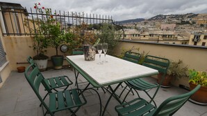 Een terras met een tafel, stoelen, plantenbakken en uitzicht op een stadsgezicht.