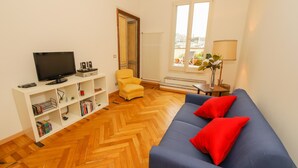 Een woonkamer met een blauwe bank, een gele fauteuil, een televisie en een boekenkast.