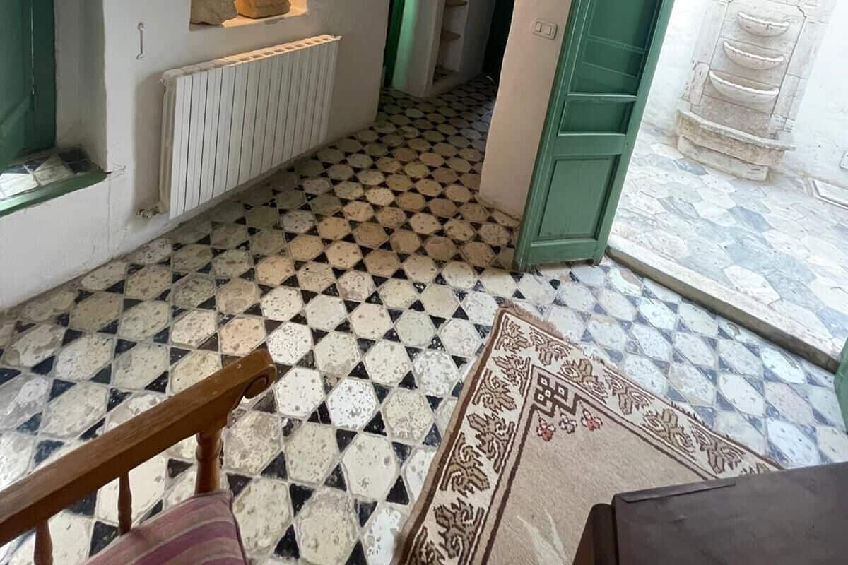 Un pasillo con suelo estampado, un radiador, una lámpara de pared y una puerta verde que da a otra habitación.