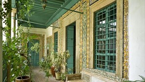 A traditional interior with a tiled wall, a large window with bars, and a cat on a bench. - Dar Hayder (Tunis)