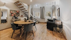 A modern living room with a wooden dining table, black chairs, a black sofa, a staircase, and a large window with curtains. - Appartamenti La Medicea (Florence)