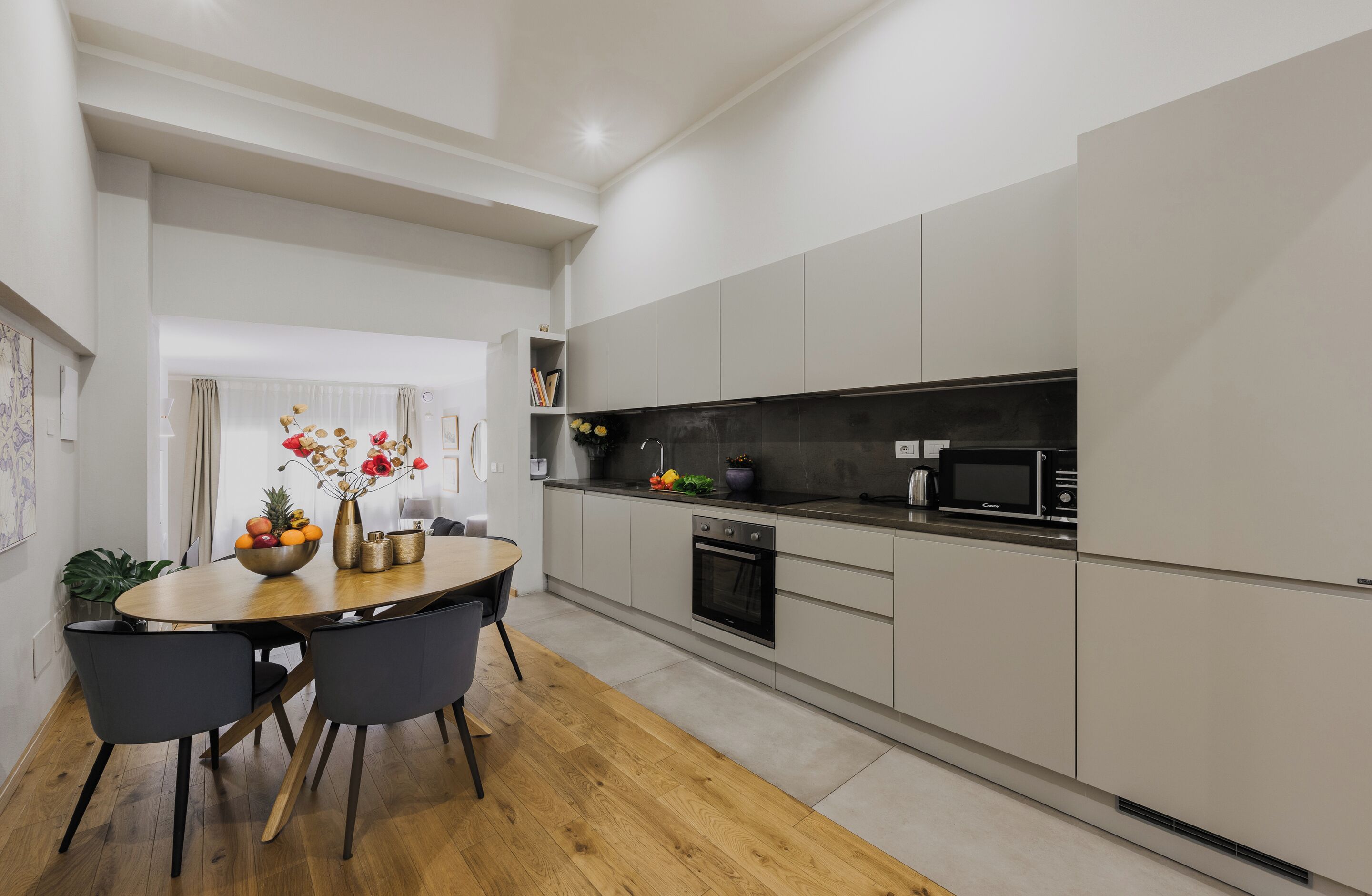 Una cocina moderna con armarios grises, un microondas negro y una mesa de comedor de madera con sillas.