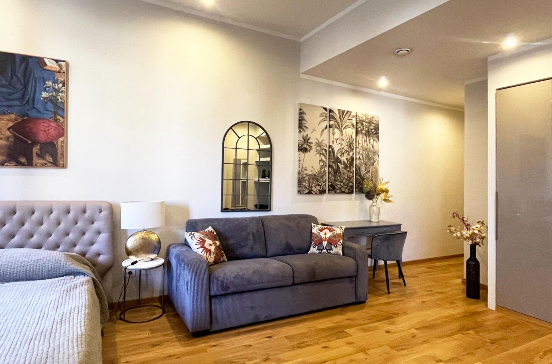 Una sala moderna con un sofá gris, un sillón capitonado y una zona de comedor con una mesa pequeña y sillas.