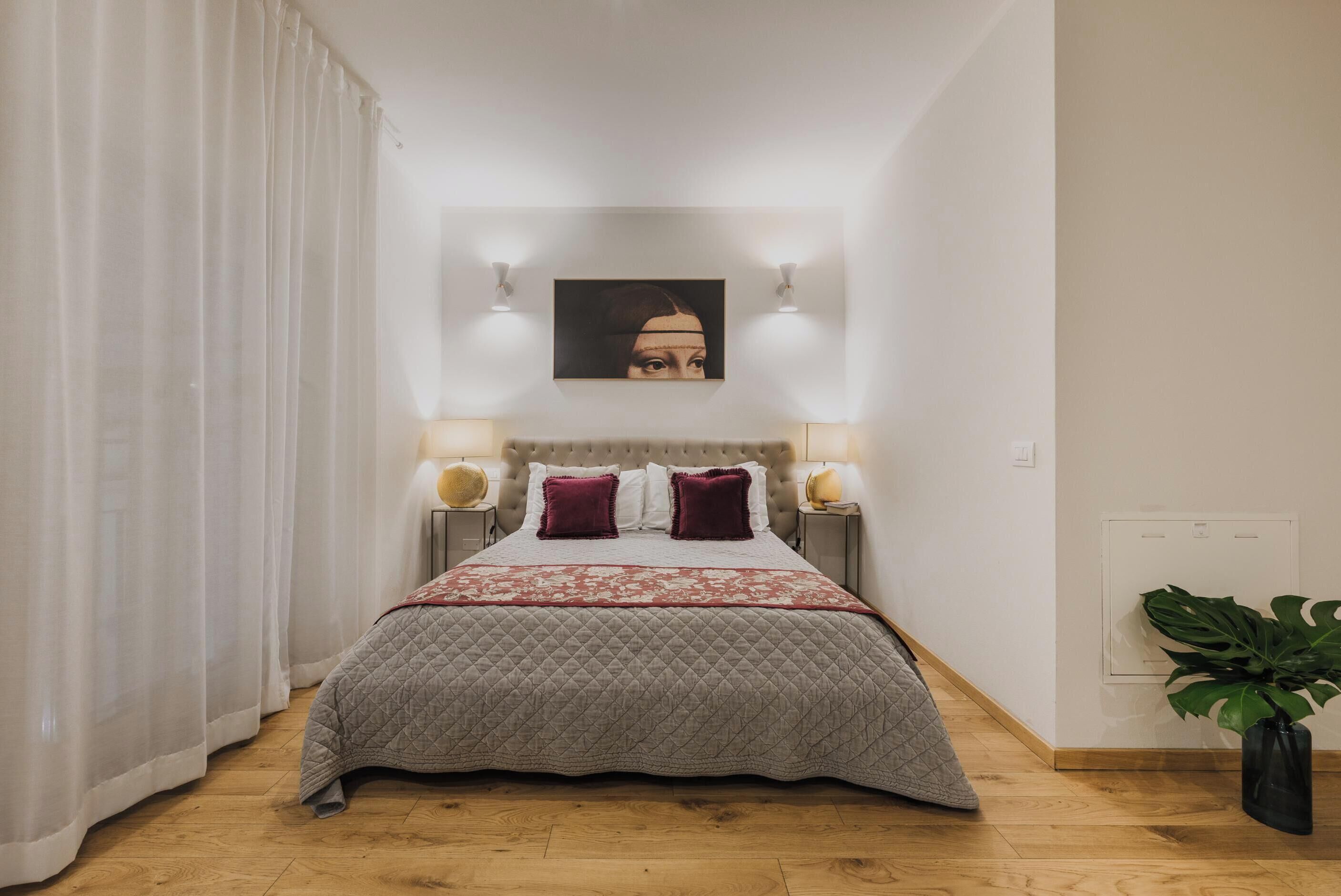 A neatly made bed with a quilted cover, two pillows, and a headboard with wall-mounted lights.