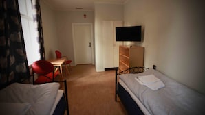Une chambre d’hôtel avec deux lits simples, un bureau avec une chaise, un téléviseur posé sur un meuble et une armoire.