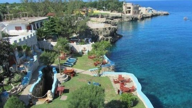 Un complejo turístico frente al mar con piscina, sillas de descanso y vistas al océano.