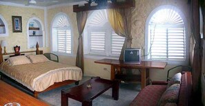 A room with two beds, a sofa, a TV on a wooden table, and large windows with shutters. - Blue Cave Castles (Negril)