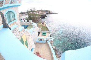 A seaside hotel with a terrace overlooking the ocean, featuring a pool, lounge chairs, and a dining area. - Blue Cave Castles (Negril)