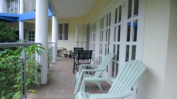 A covered outdoor area with a table and chairs, potted plants, and a view of a building with multiple windows.