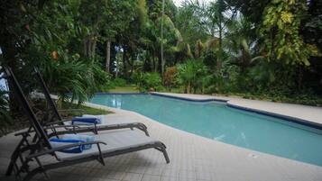 A pool area with lounge chairs and a tiled deck surrounded by lush greenery.