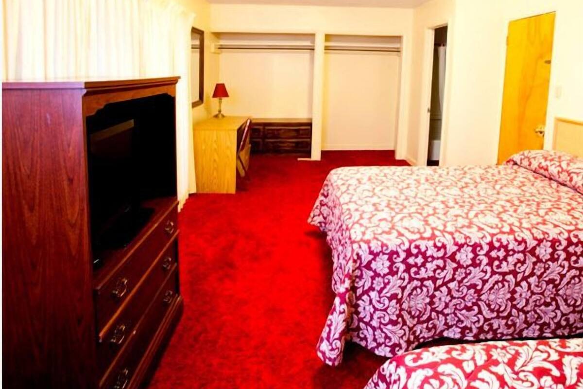 A hotel room with a large bed, a wooden dresser, a television, and a desk with a lamp.