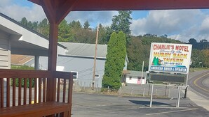 A motel with a covered parking area, a wooden bench, and a sign advertising 'Charlie’s Motel' and 'Hurry Back Tavern'. - Charlie's Motel (Frostburg)