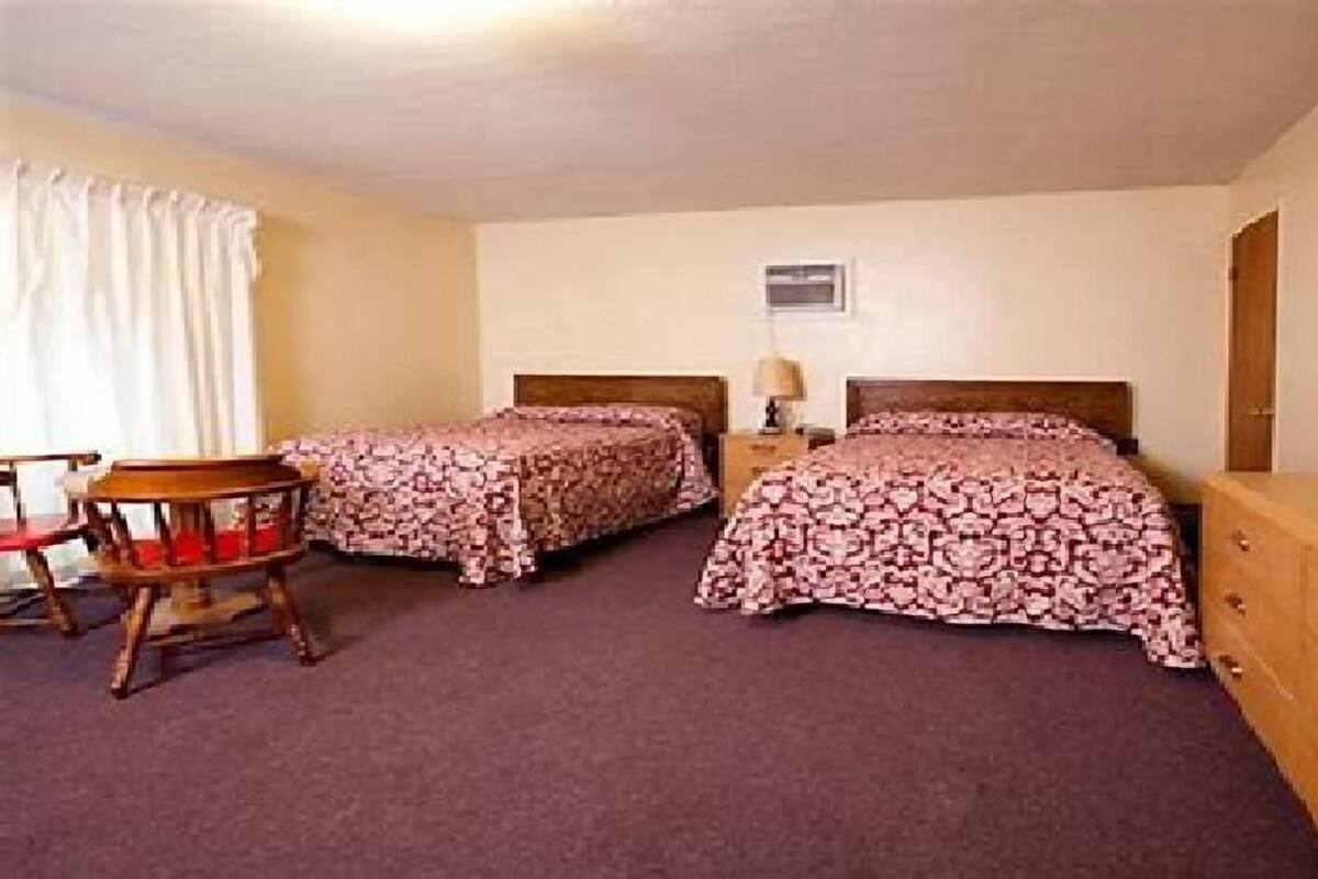 A room with two beds, a wooden chair, a nightstand with a lamp, and a dresser.