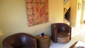 A lobby with two leather armchairs, a woven side table, and a wall-mounted abstract painting. - Casita Villa Marina (Mazatlán)