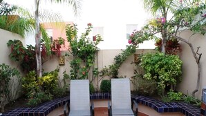 A patio with two lounge chairs, surrounded by a variety of plants and a tiled wall. - Casita Villa Marina (Mazatlán)