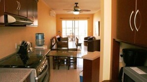 A kitchen with a stove, oven, and water dispenser. There is a dining area with a table and chairs. - Casita Villa Marina (Mazatlán)